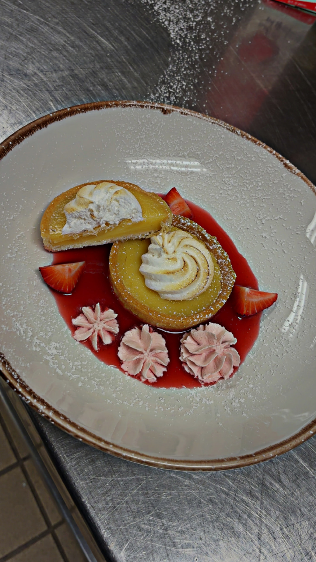 Yellow-filled tart portions topped with toasted swirls, strawberries and pink cream over red berry sauce