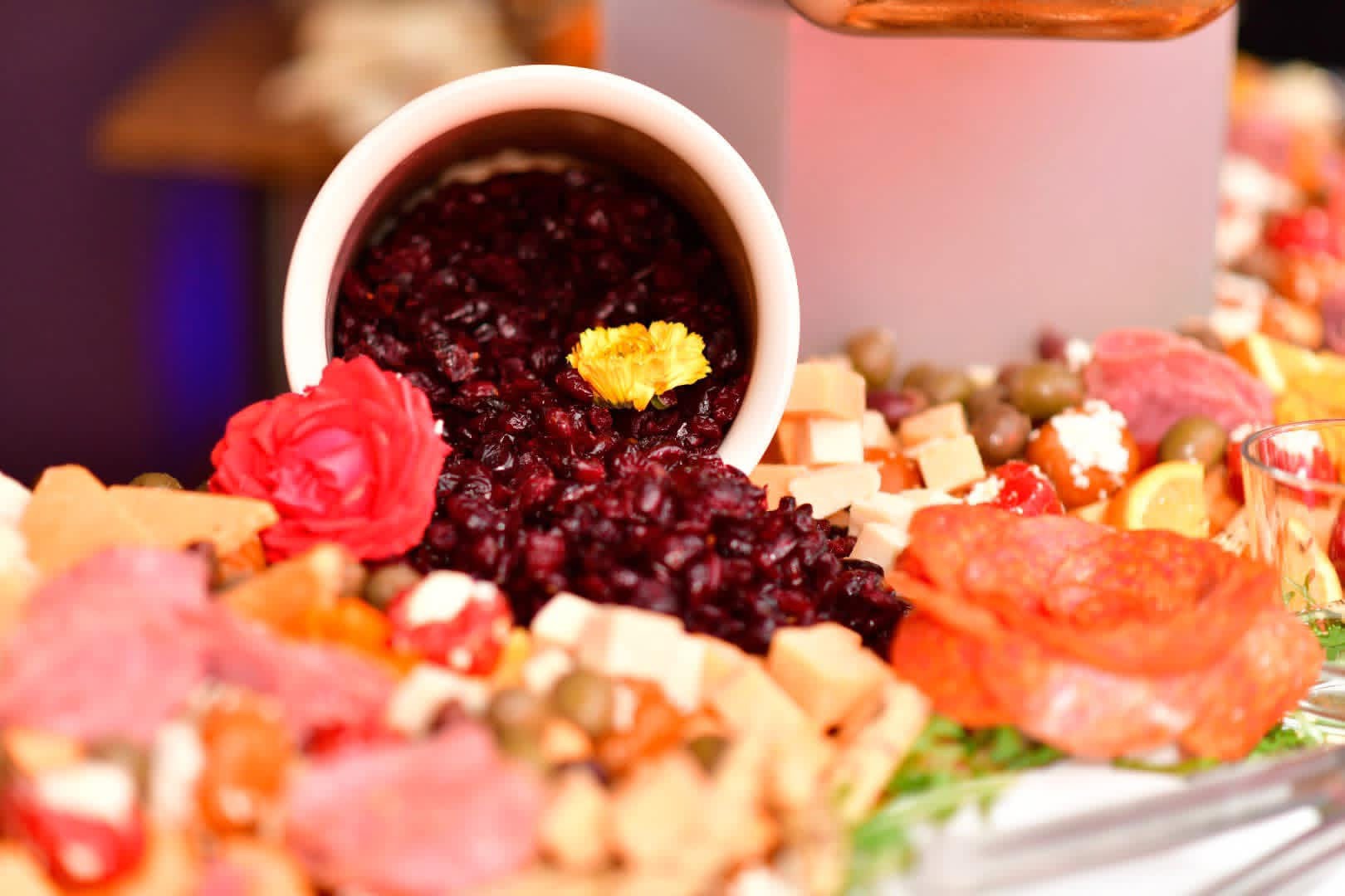 Dark fruit spread displayed with cured meats, cheese, olives and decorative flowers