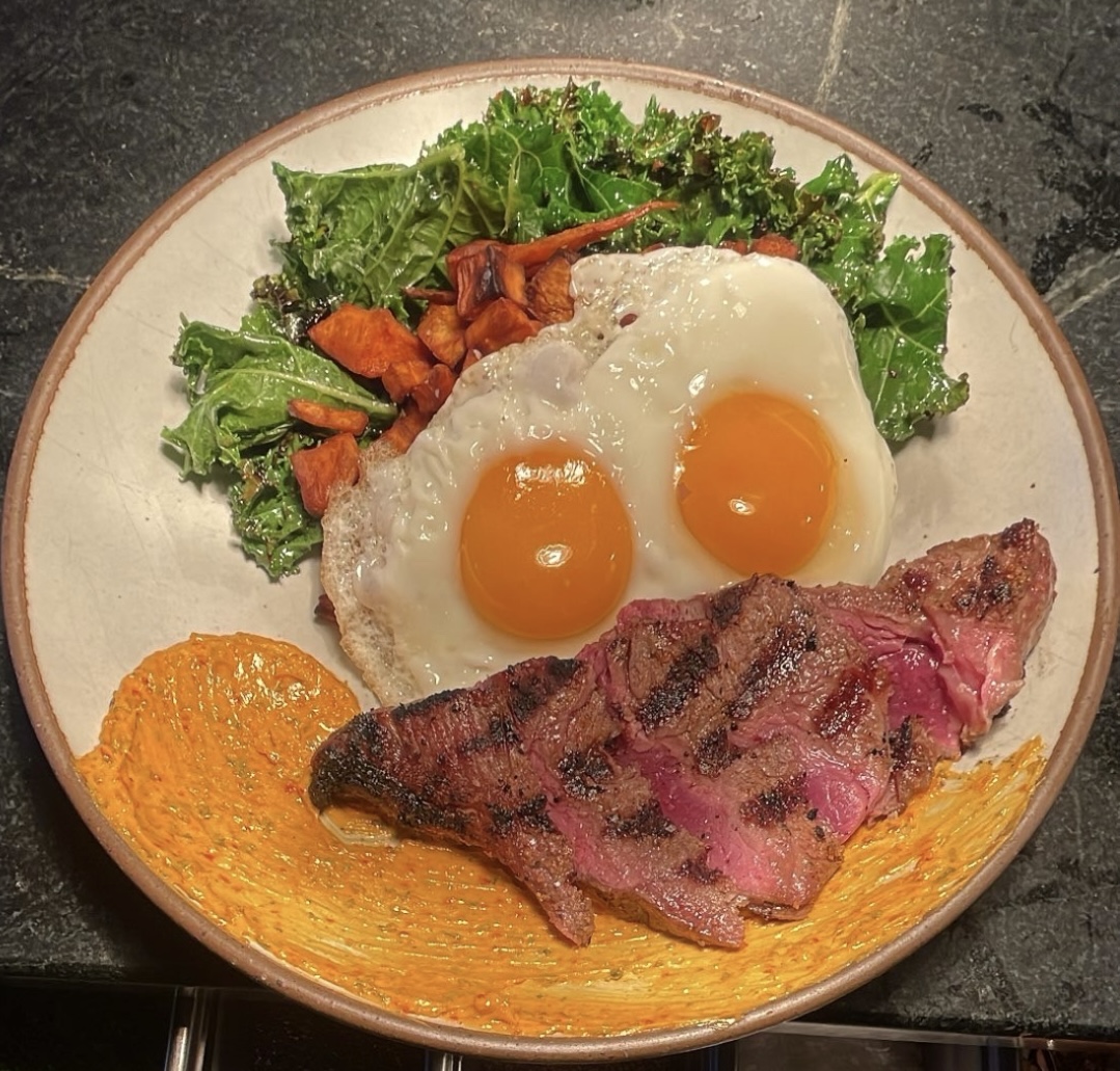 Sliced grilled steak with two sunny-side-up eggs, leafy greens, roasted vegetables and orange sauce