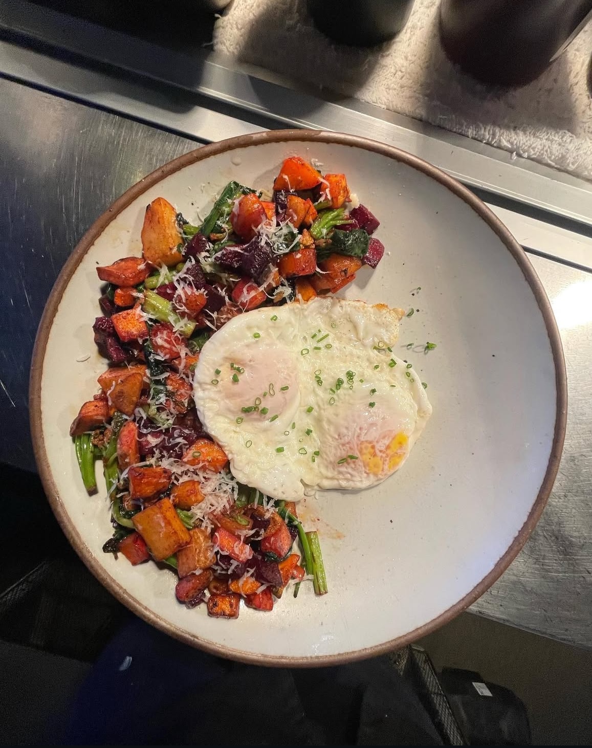 Two fried eggs with chopped chives beside colorful roasted vegetables, greens and grated cheese