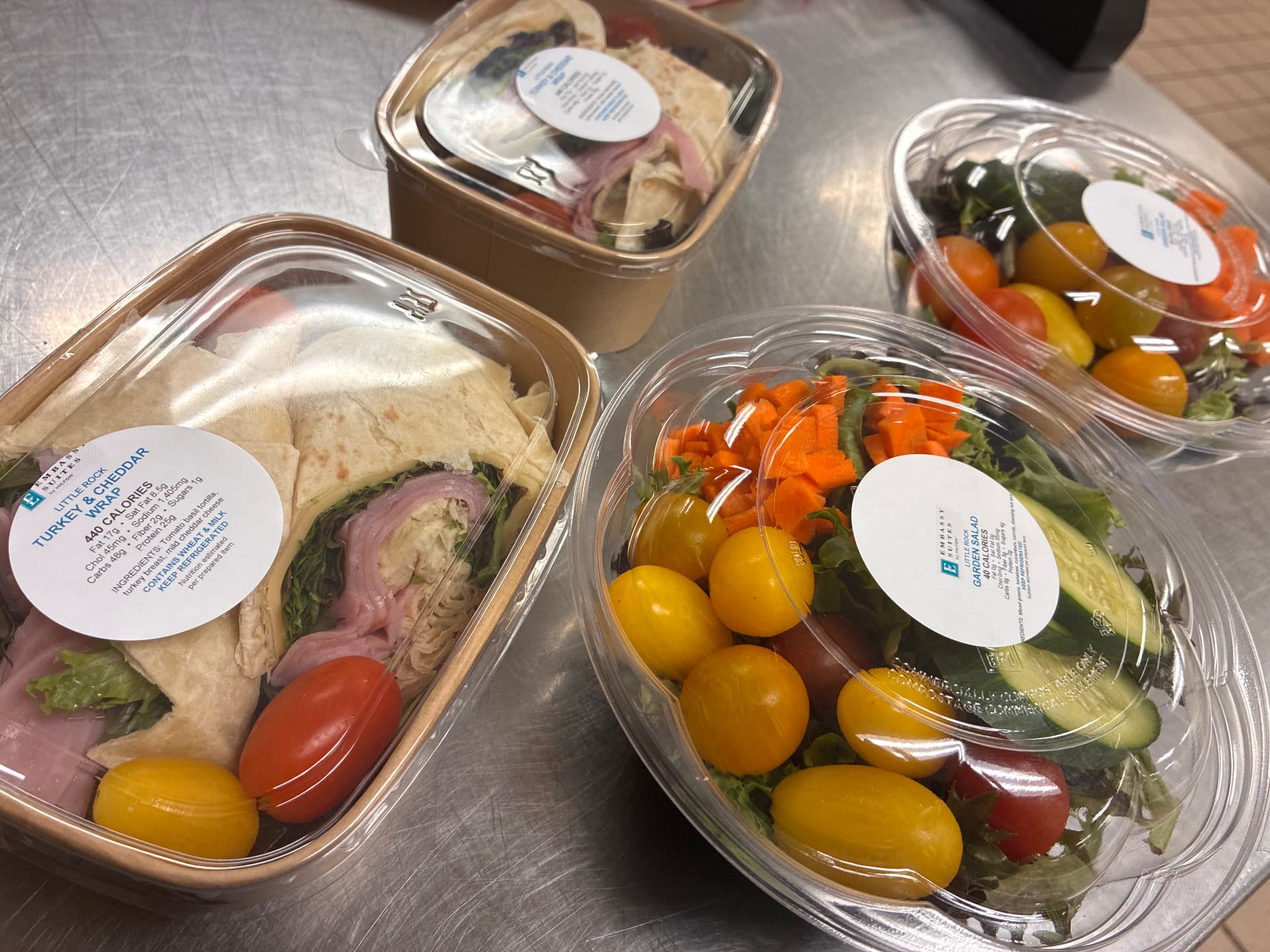 Packaged turkey and cheddar sandwiches and garden salads on a stainless-steel kitchen counter