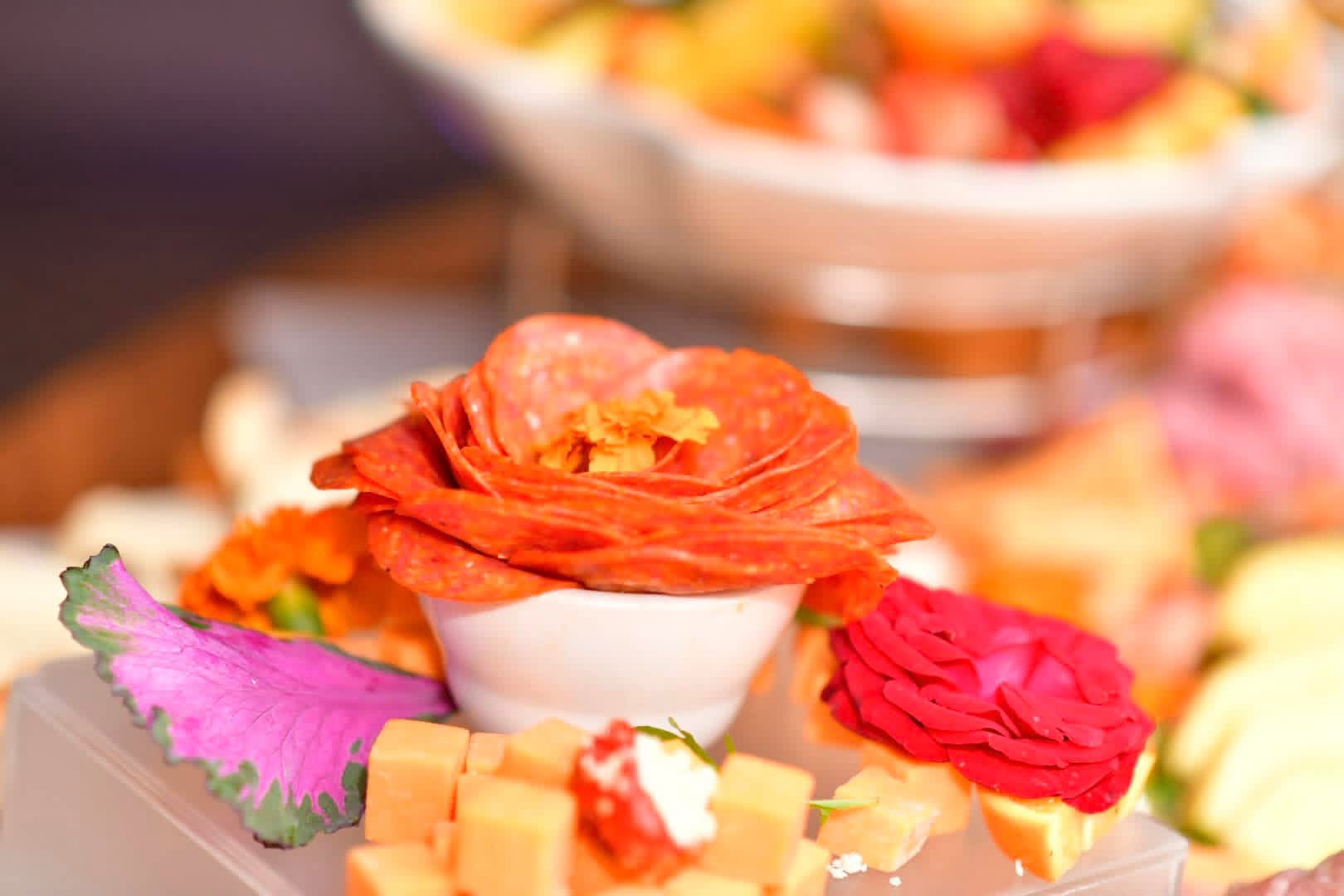 Close-up of a cured meat rose with cheese cubes and red and purple garnishes